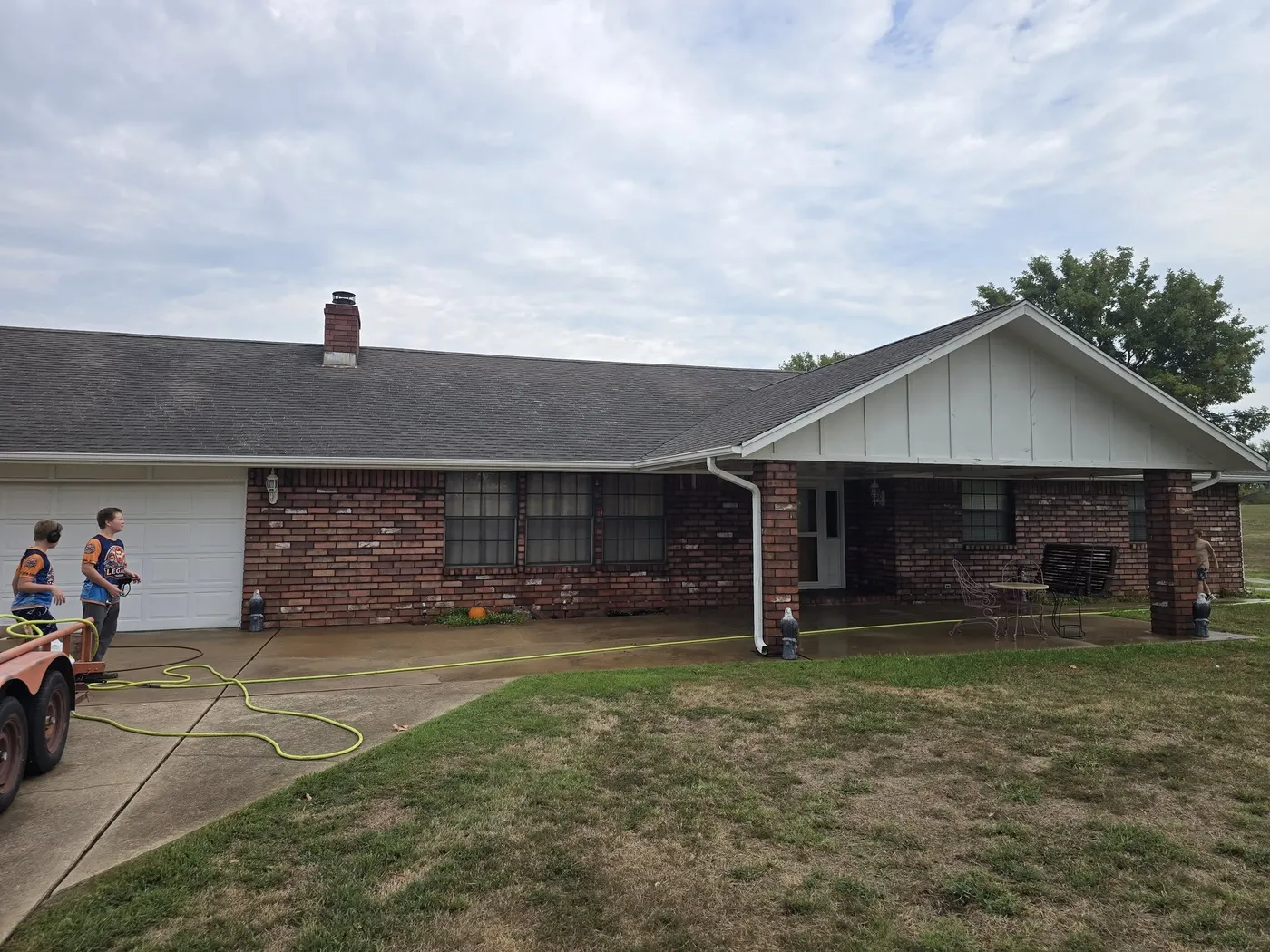 Crew washing a brick ranch home with the equipment trailer in the drive