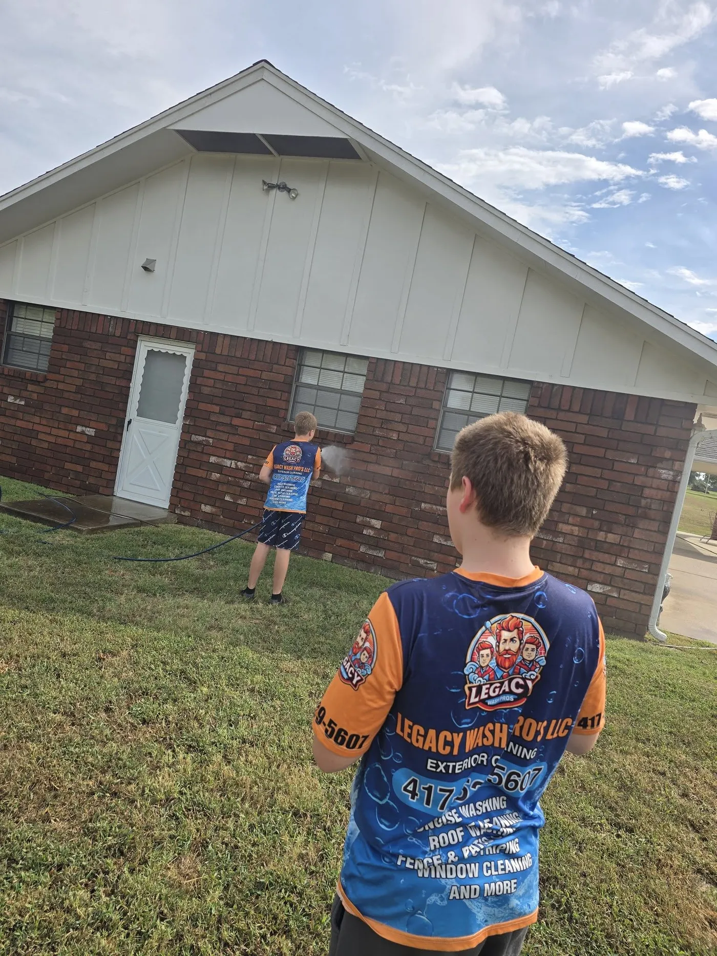 Crew member in a Legacy jersey washing a brick house